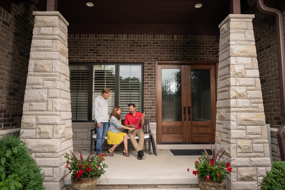 A Victors Home Solutions salesperson reviewing roofing options with a husband and wife on their front porch.