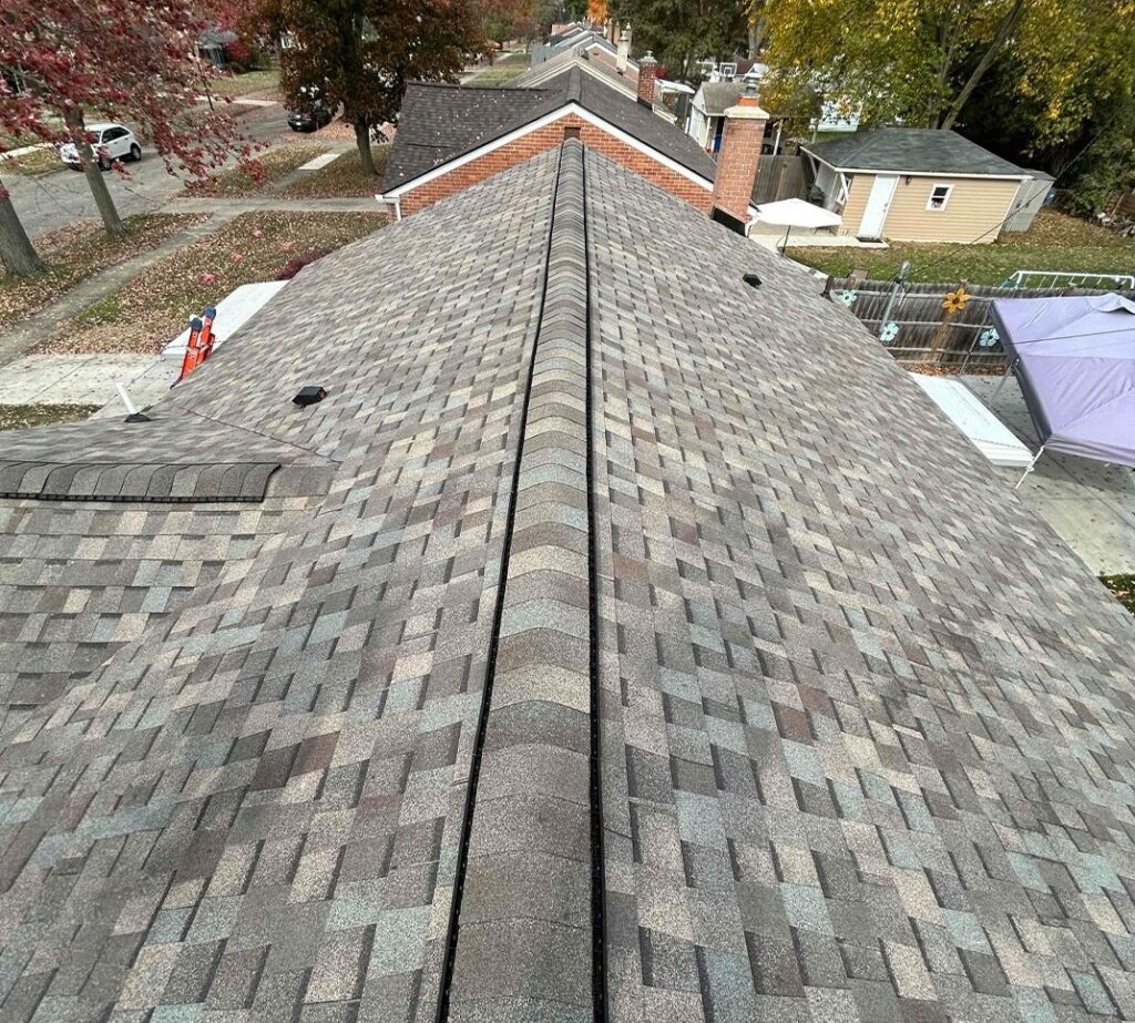 A rooftop with gray shingles, view of residential neighborhood, autumn trees, a red ladder, and a person on the left side.