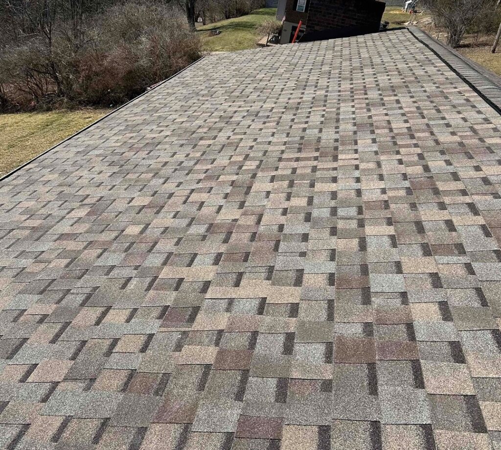 A patterned roof resembling a driveway with a building in the background, surrounded by grassy lawn and bare shrubs.