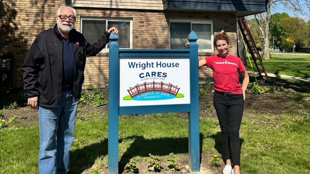 Two people stand beside a sign for Wright House CARES in Farmington Hills, labeled 